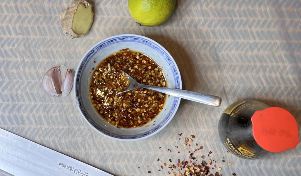 Sour and spicy sauce Eine Schüssel frisch zubereitetes Limetten-Dressing mit sichtbaren Stücken von Chili, Knoblauch und Ingwer.