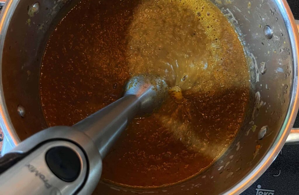 Ein Pürierstab wird in einen Topf mit brauner Bratensoße gehalten, um das Gemüse fein zu mixen.