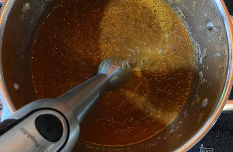 Ein Pürierstab wird in einen Topf mit brauner Bratensoße gehalten, um das Gemüse fein zu mixen.